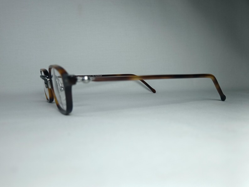 May include: Eyeglasses with a dark brown frame and tortoise shell arms. The lenses are a light amber color. The glasses are set against a white background.