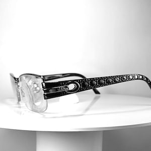 May include: Black Dior eyeglasses featuring a rectangular frame and temples adorned with a repeating circular pattern. The brand name Dior is visible on the temple hinge. The clear lenses are set within a thin black frame with integrated nose pads.