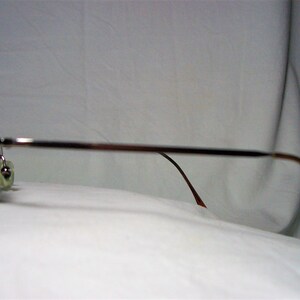 May include: Silver-toned metal eyeglasses with brown plastic arms. The glasses are on a white surface.