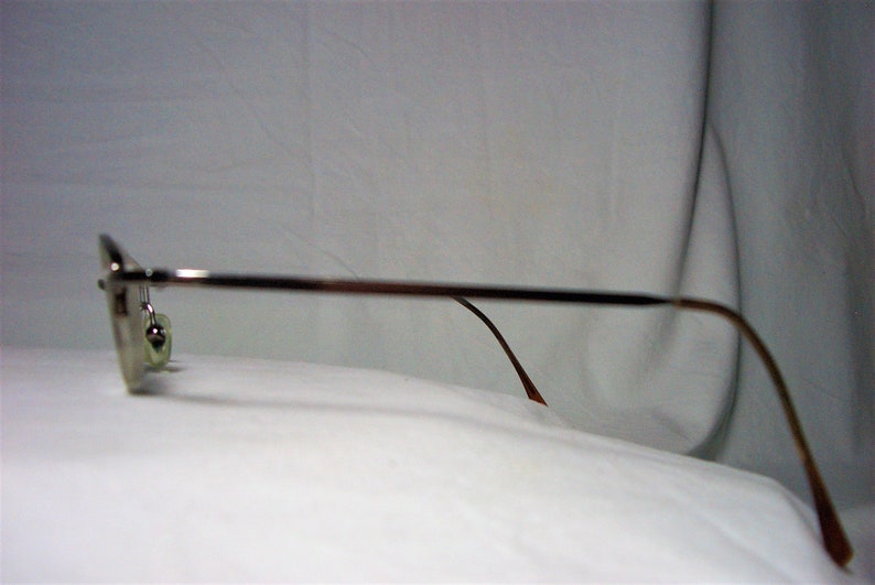 May include: Silver-toned metal eyeglasses with brown plastic arms. The glasses are on a white surface.