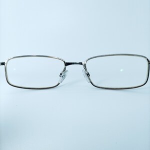 Puede incluir: Gafas rectangulares con montura plateada y lentes transparentes.