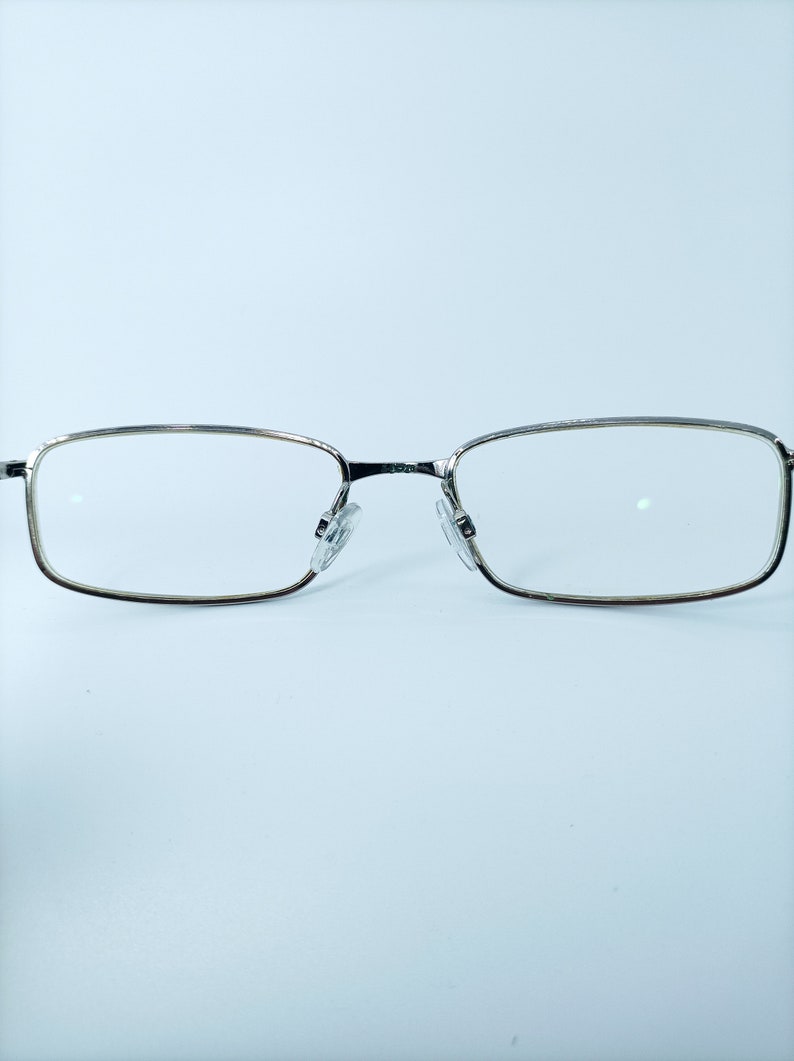 Puede incluir: Gafas rectangulares con montura plateada y lentes transparentes.