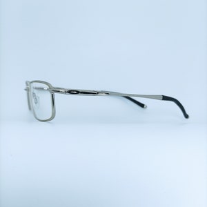 Puede incluir: Gafas de color plateado con patillas negras. Las gafas tienen una montura rectangular y lentes transparentes.