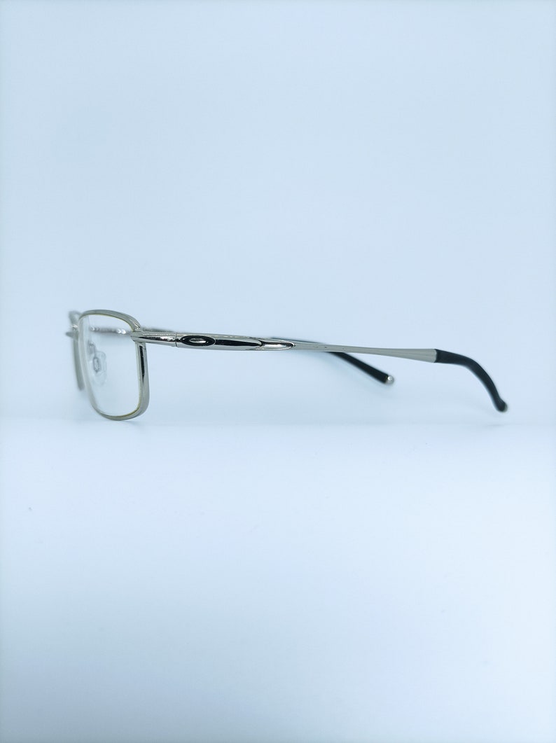 Puede incluir: Gafas de color plateado con patillas negras. Las gafas tienen una montura rectangular y lentes transparentes.