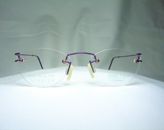 Könnte beinhalten: Lilafarbene randlose Brille mit goldenen Akzenten. Die Brille ist aus nickelallergischem Titan und trägt die Aufschrift "Synthe-Eyeze by Charmant".