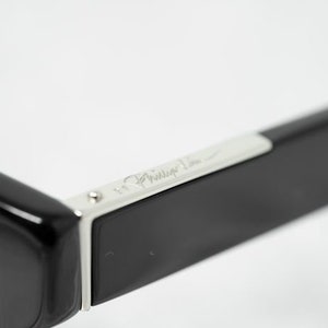 Puede incluir: Gafas de sol negras con un borde plateado y la inscripci&oacute;n "Philippe Starck" en el lateral.