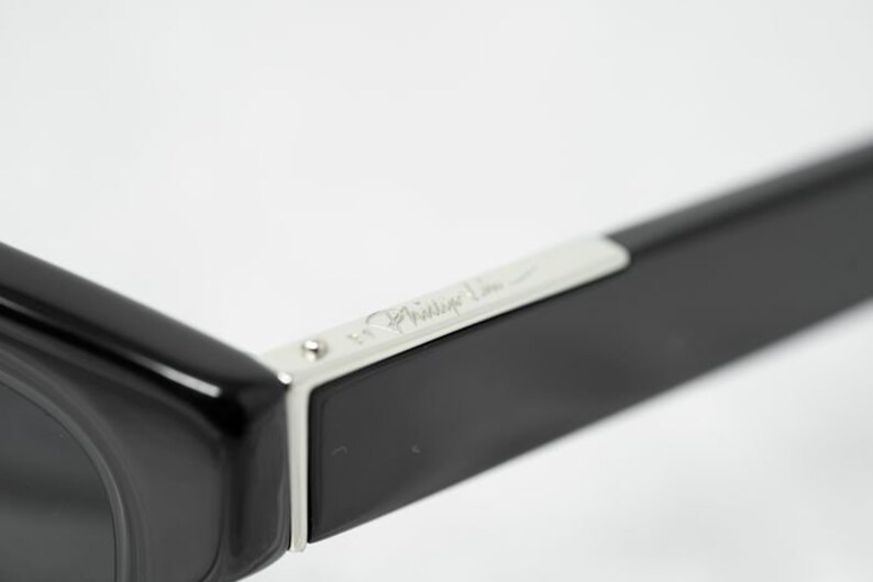 Puede incluir: Gafas de sol negras con un borde plateado y la inscripci&oacute;n "Philippe Starck" en el lateral.