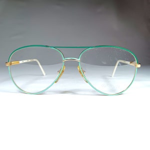 May include: Gold-rimmed glasses with a green frame and clear lenses. The brand name "Spector" is visible on the right lens.