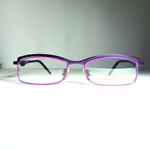 Könnte beinhalten: Lila und rosafarbene Brille mit einem goldenen Logo, auf dem "EGO NEOSTYLE" steht.