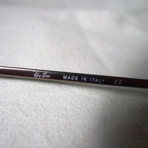 May include: Close-up of a silver metal arm of a pair of sunglasses with the text "Ray-Ban MADE IN ITALY CE" printed on it.