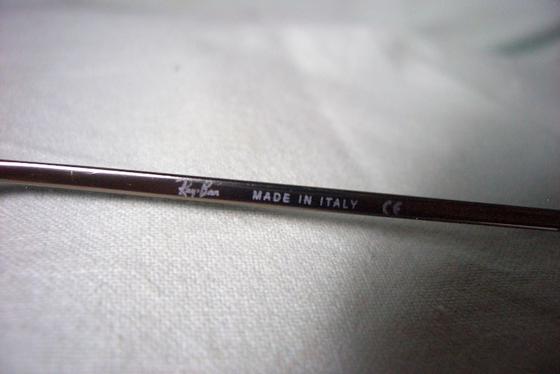May include: Close-up of a silver metal arm of a pair of sunglasses with the text "Ray-Ban MADE IN ITALY CE" printed on it.