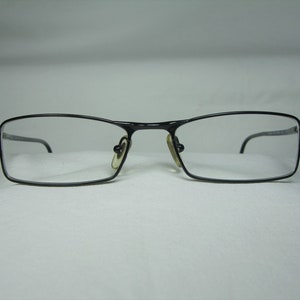 Puede incluir: Gafas rectangulares de metal negro con lentes transparentes.
