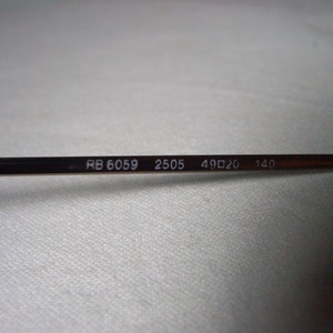 May include: Close-up of the inside of a pair of glasses with the text "RB 6059 2505 49□20 140" printed on the metal arm.