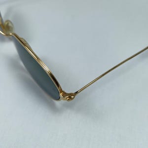 Puede incluir: Gafas de sol redondas doradas con lentes verdes y un detalle de bisagra.