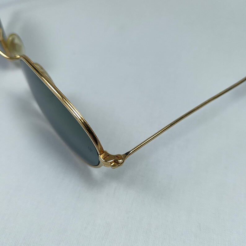 Puede incluir: Gafas de sol redondas doradas con lentes verdes y un detalle de bisagra.