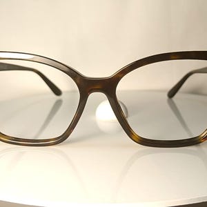 May include: A pair of tortoiseshell-patterned eyeglasses with a cat-eye shape. The frames are brown with yellow and black accents. The temples have a gold-colored accent. The lenses are clear.