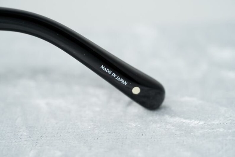 Puede incluir: Primer plano de una montura de gafas negra con el texto "MADE IN JAPAN" impreso en el lateral.
