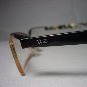 May include: Black Ray-Ban eyeglasses with a brown frame and clear lenses.