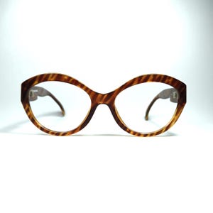 May include: A pair of tortoise shell eyeglasses with a rounded, oval shape. The glasses have clear lenses and brown, patterned frames.