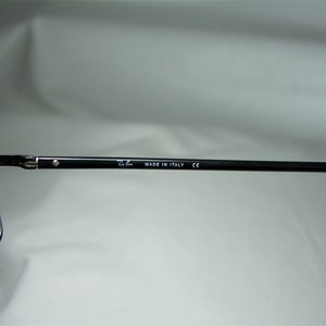 Puede incluir: Primer plano del brazo de metal negro de unas gafas con el texto "Ray-Ban MADE IN ITALY CE" impreso en &eacute;l.