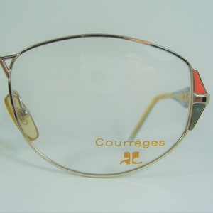 May include: Silver-toned eyeglasses with a gold-colored frame and clear lenses. The glasses have a red and green accent on the side and the text "Courr&egrave;ges" and "CC" on the frame.