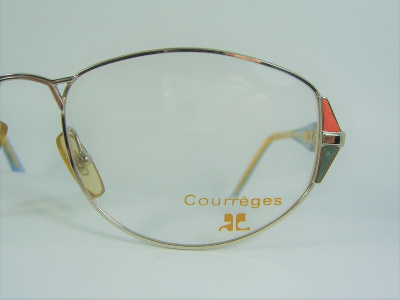 May include: Silver-toned eyeglasses with a gold-colored frame and clear lenses. The glasses have a red and green accent on the side and the text "Courr&egrave;ges" and "CC" on the frame.