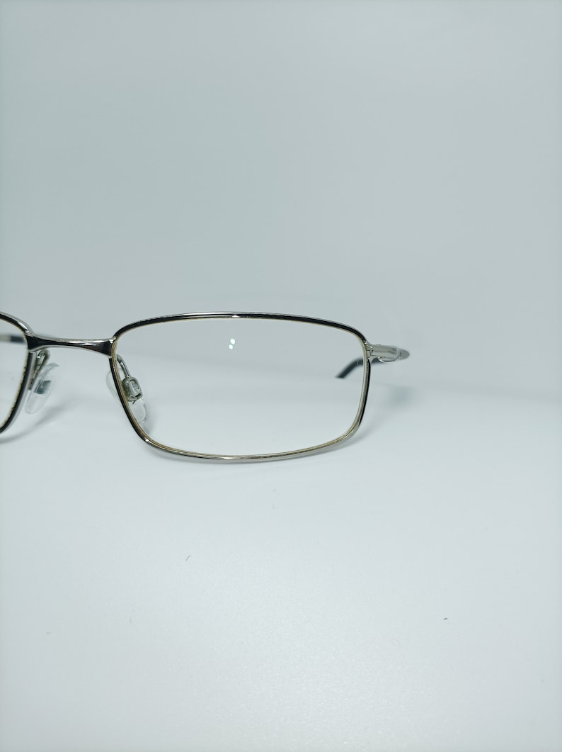 Puede incluir: Gafas rectangulares con montura plateada y lentes transparentes.