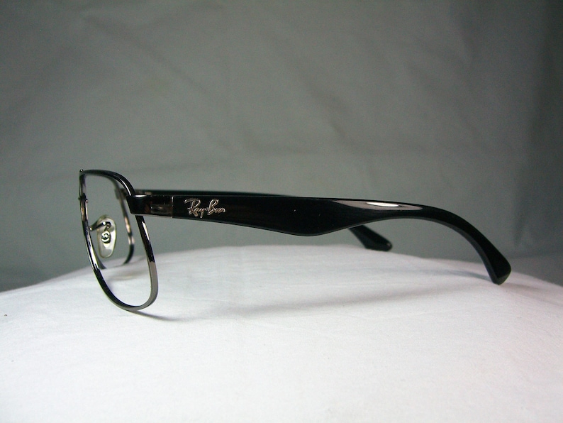 K&ouml;nnte beinhalten: Schwarze und silberne Ray-Ban Brille mit einem d&uuml;nnen Metallrahmen und schwarzen Kunststoffb&uuml;geln.