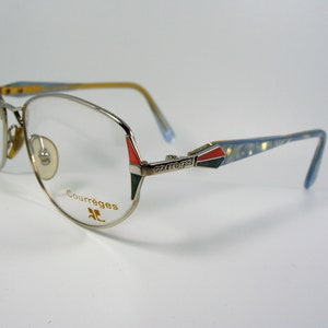 May include: Silver-toned eyeglasses with a blue and gold patterned arm. The frame has a red, black, and green accent at the temple. The brand name "Courr&egrave;ges" is printed in gold on the frame.