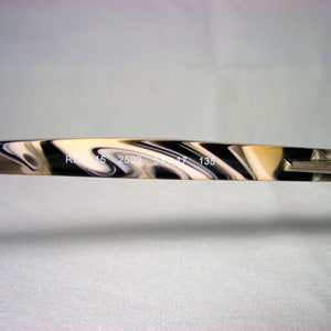 May include: Close-up of the arm of a pair of eyeglasses with a black and white marbled pattern. The text "RB 2509 53 17 135" is printed on the arm.