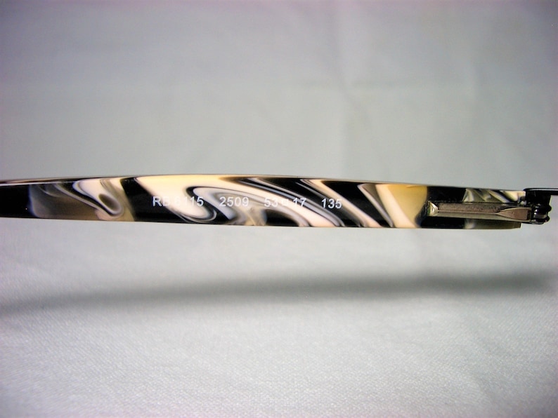 May include: Close-up of the arm of a pair of eyeglasses with a black and white marbled pattern. The text "RB 2509 53 17 135" is printed on the arm.