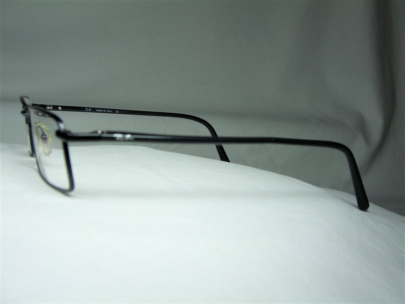 Puede incluir: Gafas de metal negro con un fino marco de metal y lentes transparentes. Las gafas est&aacute;n apoyadas sobre una superficie blanca.