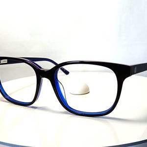 May include: Black eyeglasses with a blue inner frame and temples. The glasses have a rectangular shape with a rounded edge. The lenses are clear, and the frame is made of a glossy material.