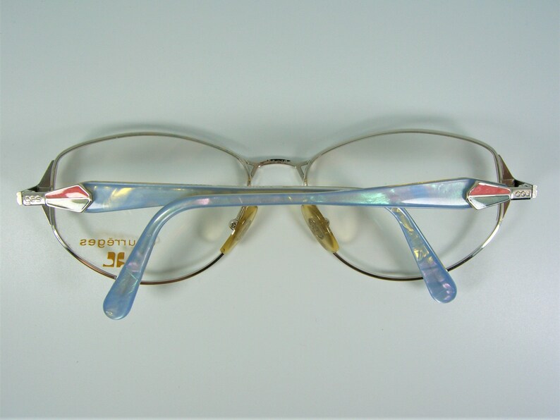 May include: Silver-toned eyeglasses with blue and white patterned arms. The arms have a red and white accent at the end. The text "Jill&eacute; edges" is printed on the left arm.