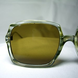 Może przedstawiać: Okulary przeciwsłoneczne z przezroczystą plastikową oprawką i brązowymi szkłami. Okulary mają retro styl.