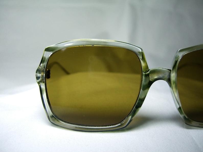 Może przedstawiać: Okulary przeciwsłoneczne z przezroczystą plastikową oprawką i brązowymi szkłami. Okulary mają retro styl.