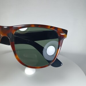 May include: Sunglasses with a tortoiseshell pattern frame and dark green lenses. The sunglasses have a classic, rectangular shape with black arms. The frame features a mix of brown and amber hues.
