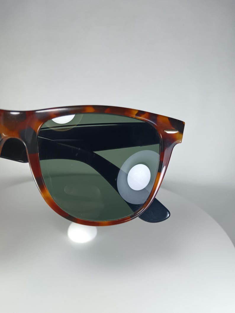 May include: Sunglasses with a tortoiseshell pattern frame and dark green lenses. The sunglasses have a classic, rectangular shape with black arms. The frame features a mix of brown and amber hues.