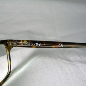 May include: Tortoise shell eyeglasses with clear lenses and silver accents. The arms of the glasses are marked "Ray-Ban" and "CE".