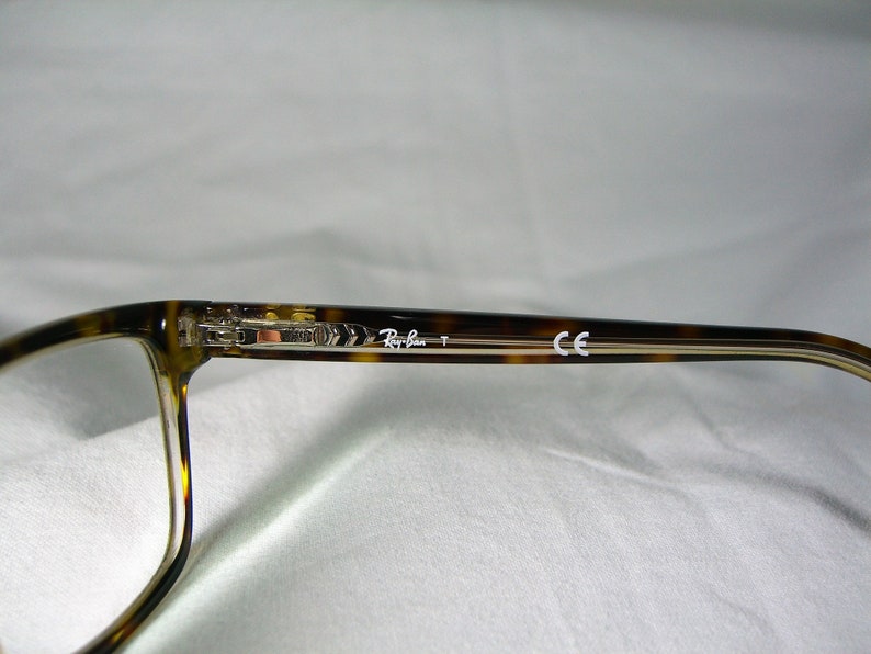 May include: Tortoise shell eyeglasses with clear lenses and silver accents. The arms of the glasses are marked "Ray-Ban" and "CE".