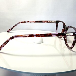 Peut inclure: Lunettes avec un motif &eacute;caille de tortue dans les tons marron, violet et blanc. Les lunettes ont une monture rectangulaire et la marque "ROXY" est visible sur le c&ocirc;t&eacute;. Les lunettes reposent sur une surface blanche.