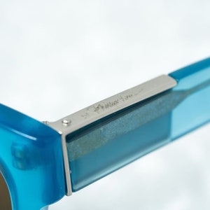 K&ouml;nnte beinhalten: Nahaufnahme einer blauen Sonnenbrille mit einem silbernen Metallgelenk. Das Gelenk tr&auml;gt die Gravur "Made in Italy".
