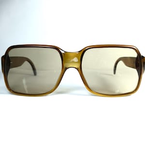 May include: Vintage square-framed sunglasses with a light brown tint. The frames are a translucent amber color, with a classic, retro design. The lenses are a light brown color, offering a vintage aesthetic.