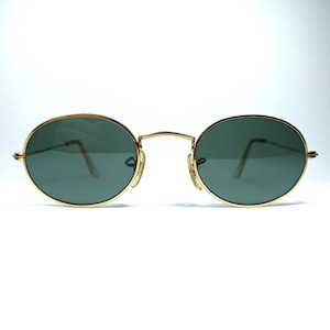 Puede incluir: Gafas de sol ovaladas con montura dorada y lentes verde oscuro.