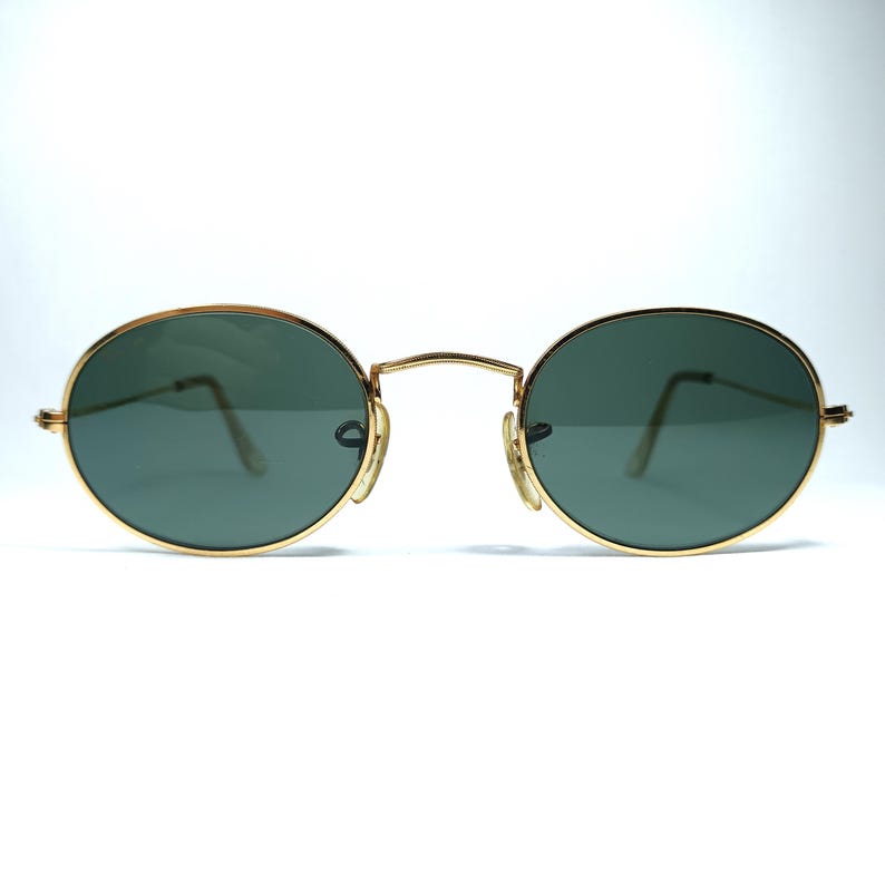 Puede incluir: Gafas de sol ovaladas con montura dorada y lentes verde oscuro.