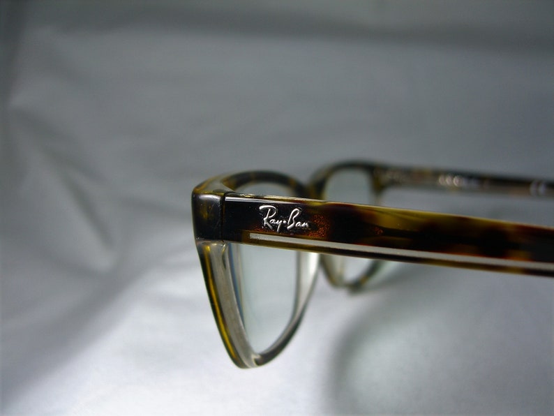 May include: Close-up of a pair of tortoiseshell eyeglasses with a silver Ray-Ban logo on the frame.