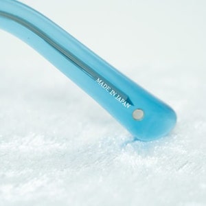 K&ouml;nnte beinhalten: Nahaufnahme des blauen Plastikb&uuml;gels einer Sonnenbrille. Der B&uuml;gel ist mit den Worten "MADE IN JAPAN" gekennzeichnet.