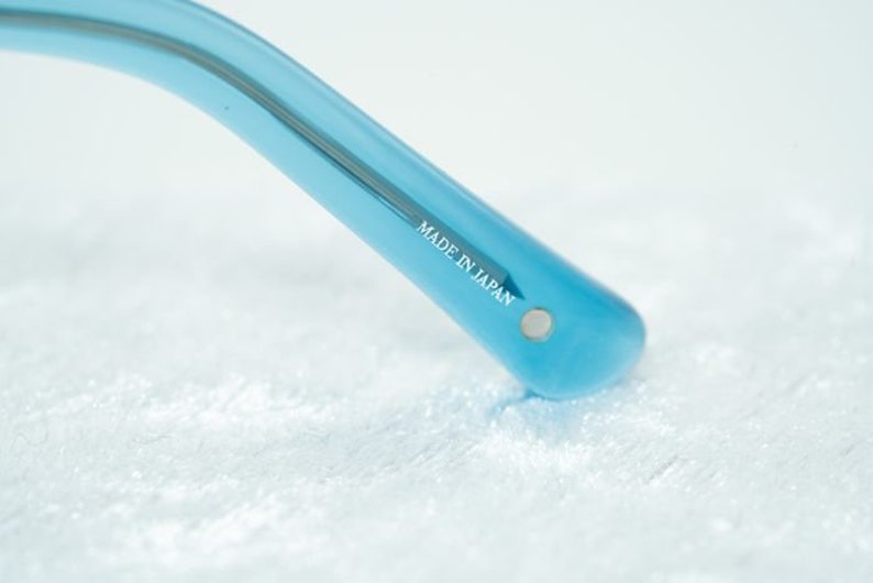 K&ouml;nnte beinhalten: Nahaufnahme des blauen Plastikb&uuml;gels einer Sonnenbrille. Der B&uuml;gel ist mit den Worten "MADE IN JAPAN" gekennzeichnet.