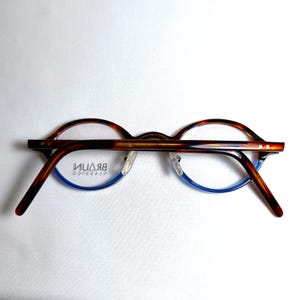 May include: Brown and blue eyeglasses with a tortoiseshell pattern on the upper frame and temples. The lower frame is blue. The brand name "BRAUN CLASSICS" is visible on the lens.