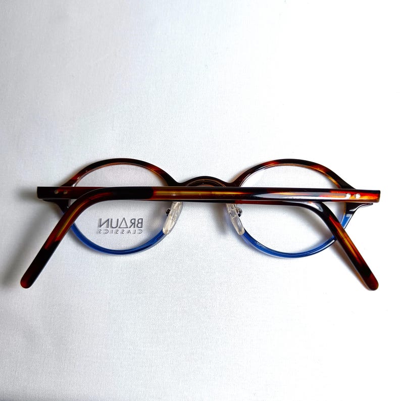 May include: Brown and blue eyeglasses with a tortoiseshell pattern on the upper frame and temples. The lower frame is blue. The brand name "BRAUN CLASSICS" is visible on the lens.